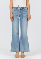 A model wearing light-wash blue flare jeans with a drawstring waist, paired with a white top and beige heels, shown against a plain white studio background.