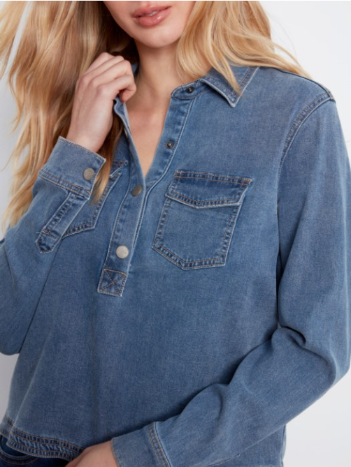 A close-up of a woman wearing a blue denim long-sleeve button-up shirt with chest pockets, shown against a plain light background.