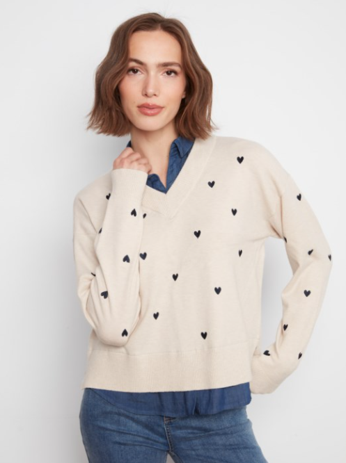 Woman wearing a cream sweater with black heart patterns on a white background