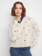 Woman wearing a cream sweater with black heart patterns on a white background