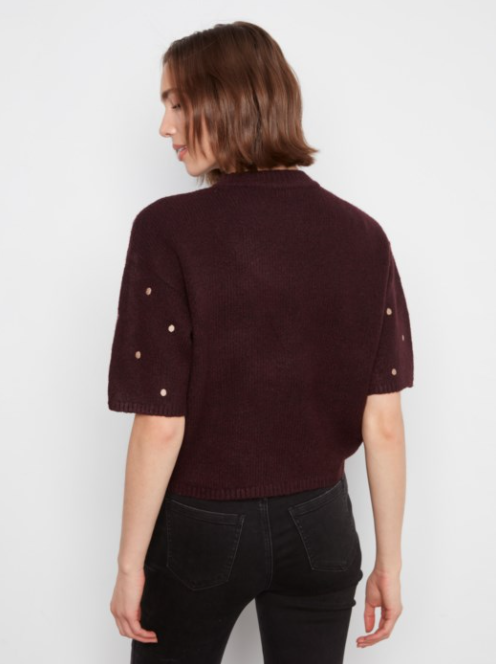 A woman shown from the back wearing a dark burgundy knit short-sleeve top with gold button accents on the sleeves, paired with black jeans, against a plain white background.