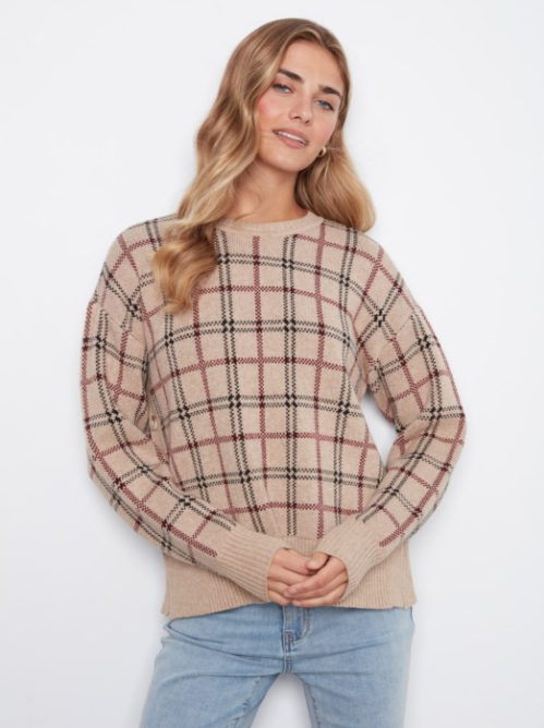 A woman wearing a beige crewneck sweater with a brown and black plaid pattern, paired with light blue jeans, against a plain white background.