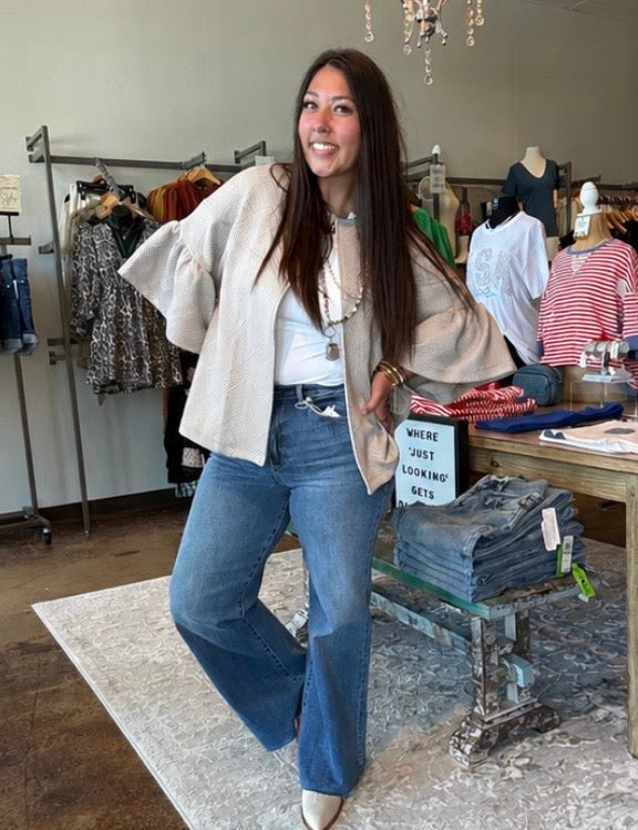 Woman posing in a clothing store wearing a beige jacket and blue jeans.
