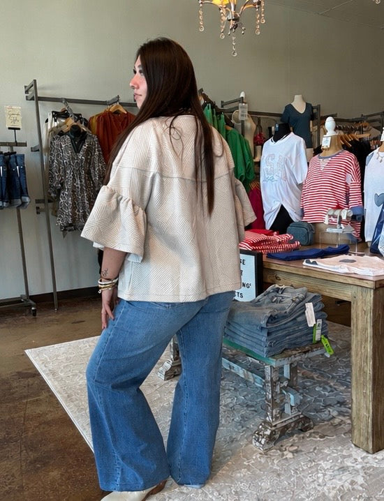 Woman in a beige jacket and blue jeans standing in a clothing store.