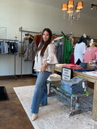 Woman standing in a clothing store with racks of clothes and a counter.