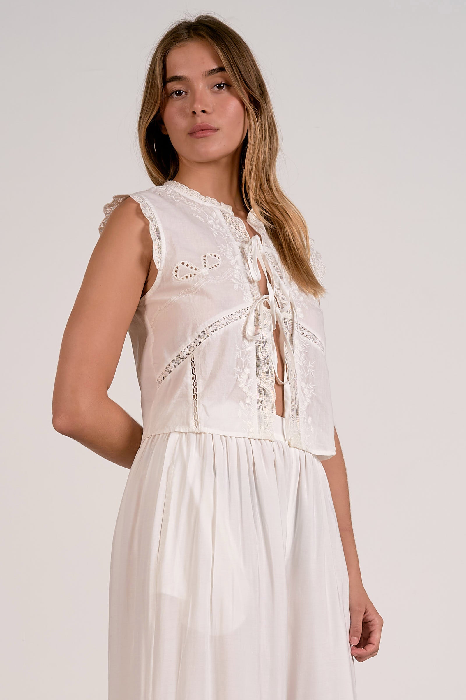 Woman wearing a white sleeveless dress with lace details on a plain background