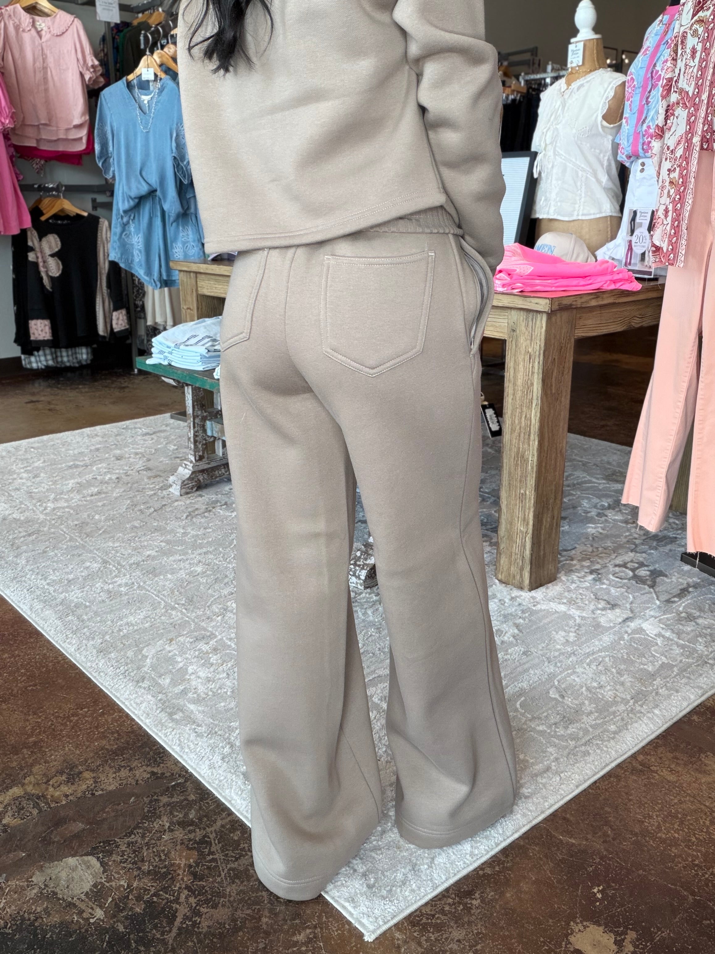 A person wearing a beige knit matching set consisting of a cropped long-sleeve top and wide-leg pants, shown from the back in a clothing store.