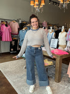 A woman modeling a striped long-sleeve crop top and wide-leg blue jeans with rolled cuffs, standing inside a clothing boutique.