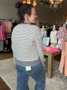 A woman wearing a cream and navy blue horizontally striped knit sweater and blue jeans, standing inside a clothing boutique.