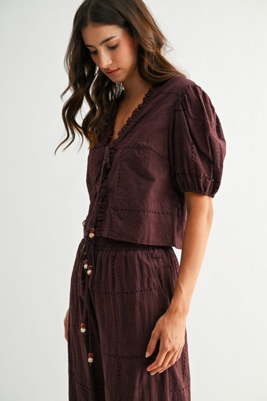 Model wearing brown embroidered puff sleeve tie-front top, side view
