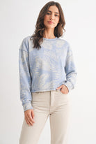 Model wearing dusty blue tropical print French terry crewneck sweatshirt, front view with ribbed cuffs