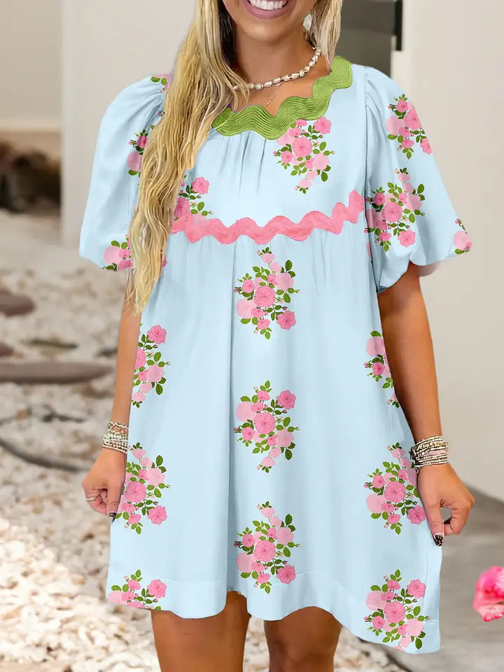 Woman wearing a light blue dress with pink floral embroidery on a neutral background